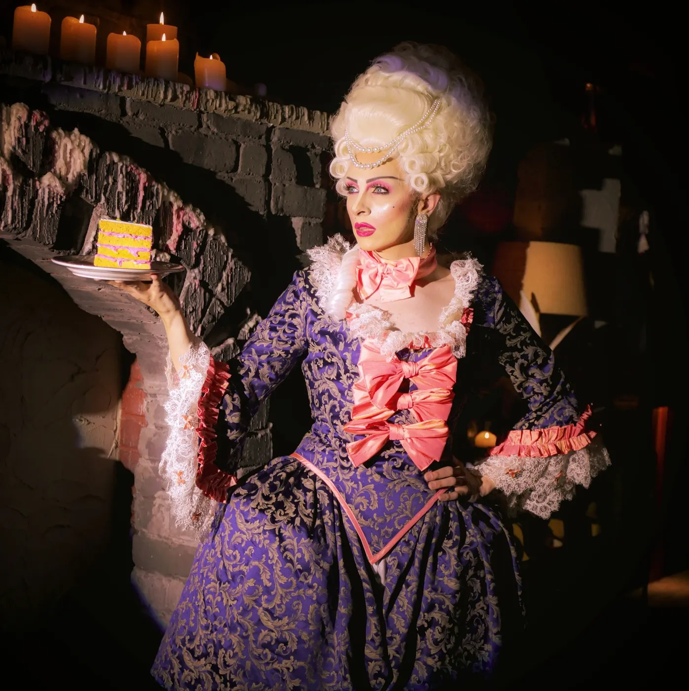 Corseted performer in period costume holds a cake in a candlelit room