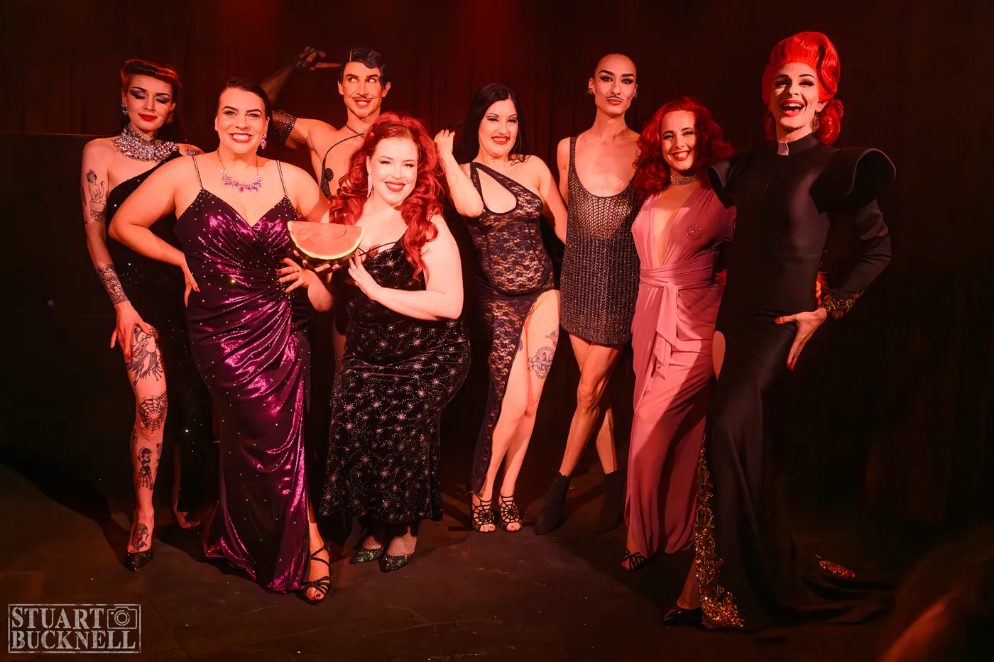 Cabaret cast lines up in corsets and gowns in a dark room