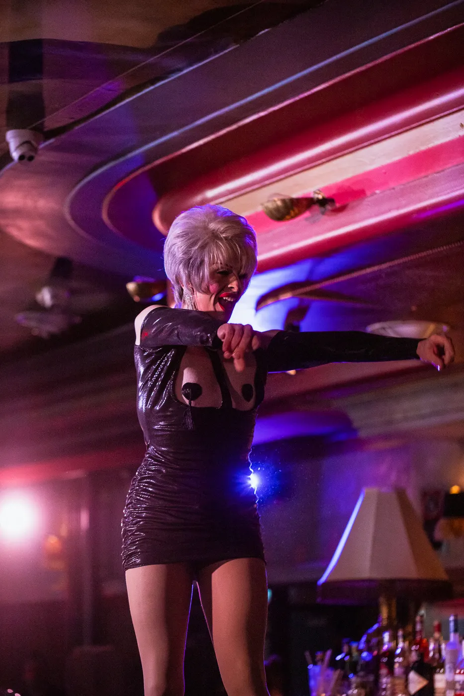 Performer in a black dress sings under pink and purple stage lighting